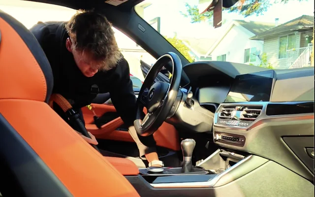 Crawford vacuuming the interior of a BMW M4 with orange leather seats