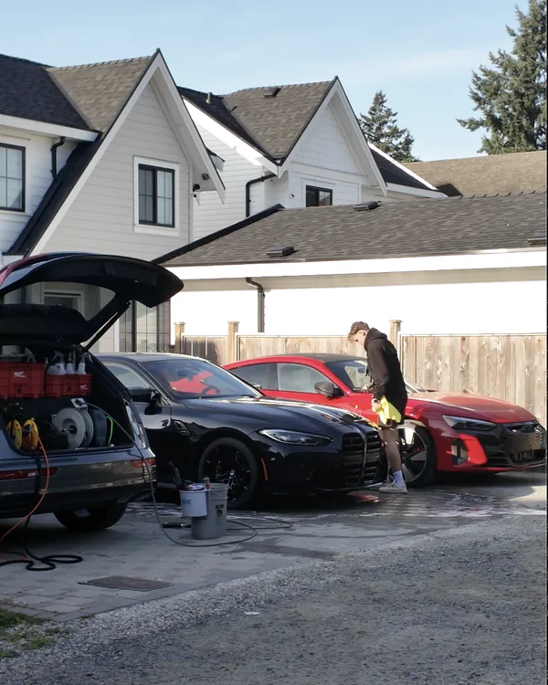 Crawford working on a red Audi RS e-tron GT next to a black BMW M4, with the Vancouver Auto Spa equipment set up in an SUV trunk